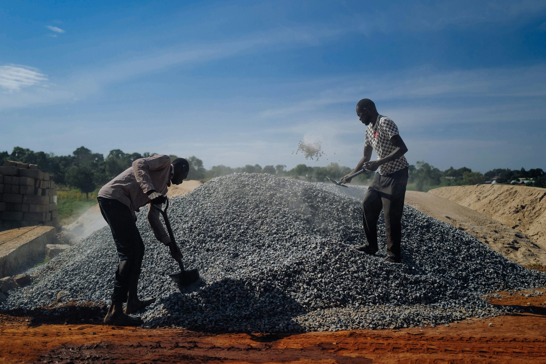 Two workers shovelling aggregate at a road construction site